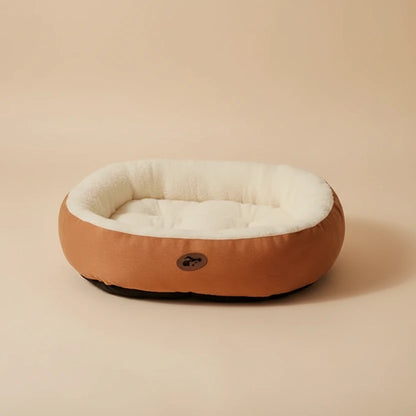 Round pet bed with brown exterior and white interior on a beige background